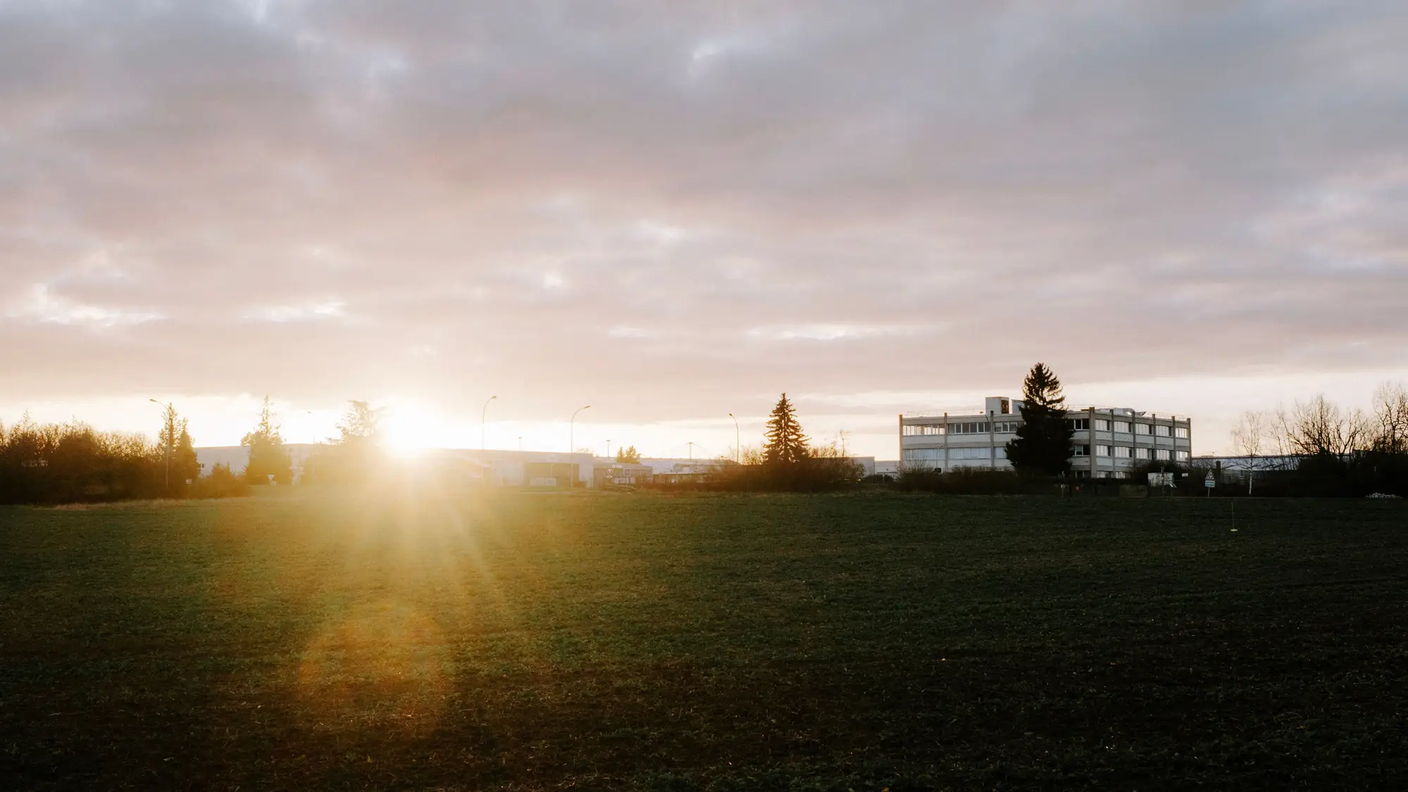 Open ground at the edge of town at dusk, with low buildings beyond the field
